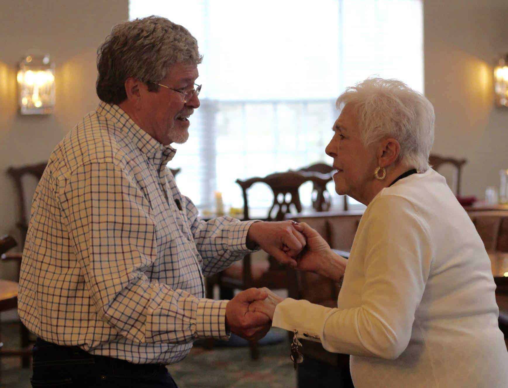 Two seniors are holding hands in the dining room