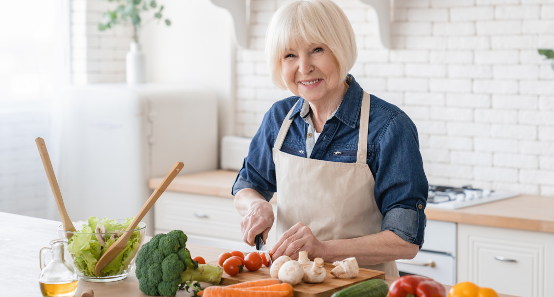 An elderly woman in denim is cutting vegetables in the kitchen