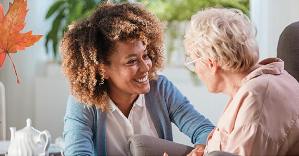 A woman in light blue comforts and smiles with an elderly woman