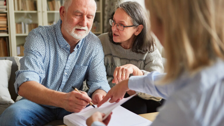 An elderly man is holding a pen and looking to sign a paper