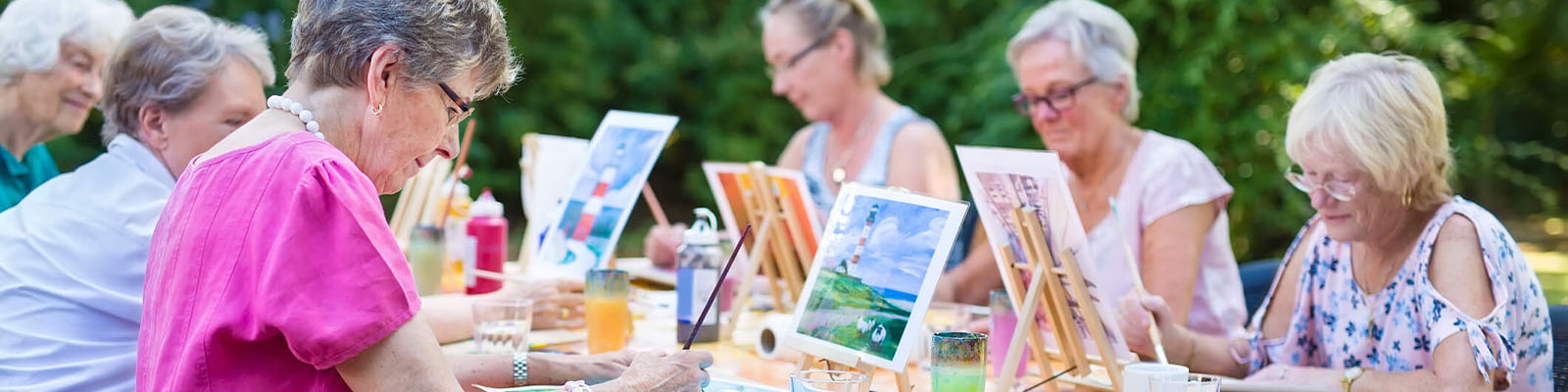 Senior women gathered around a table outdoors while painting