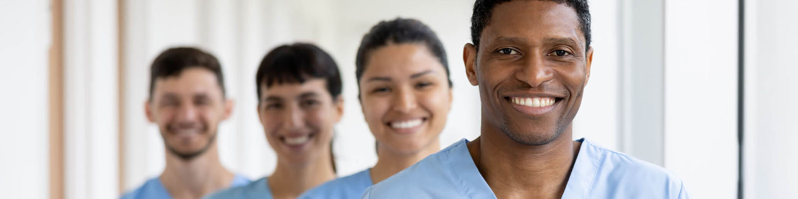 Four male and female nursing assistants wearing blue scrubs and smiling