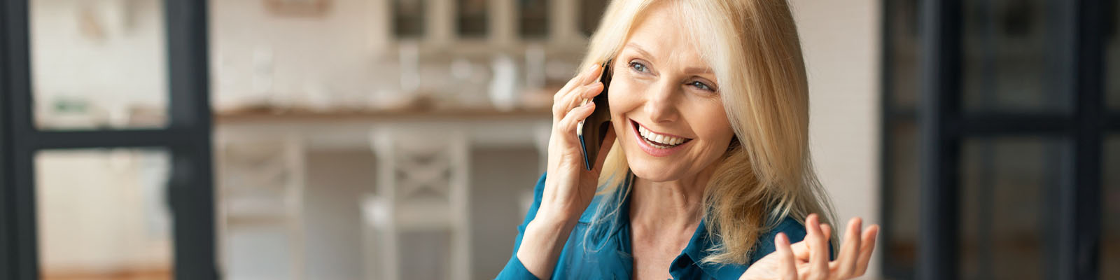 A mature woman with blonde hair smiling while talking on her smartphone