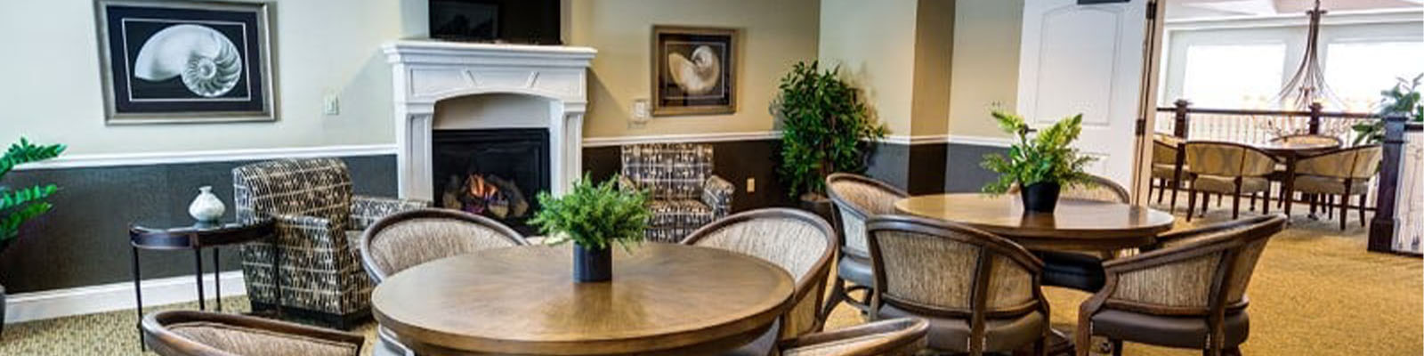 Photo of a community space with round tables and a fireplace at Meadow Brook Senior Living