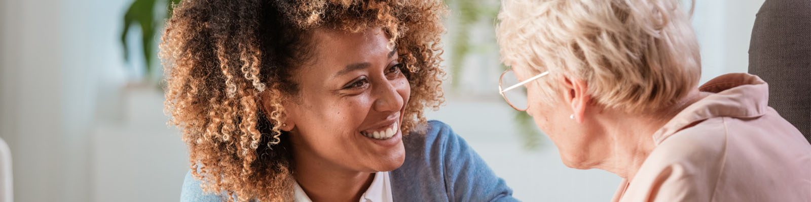 A female nursing assistant smiling and looking at her elderly female patient